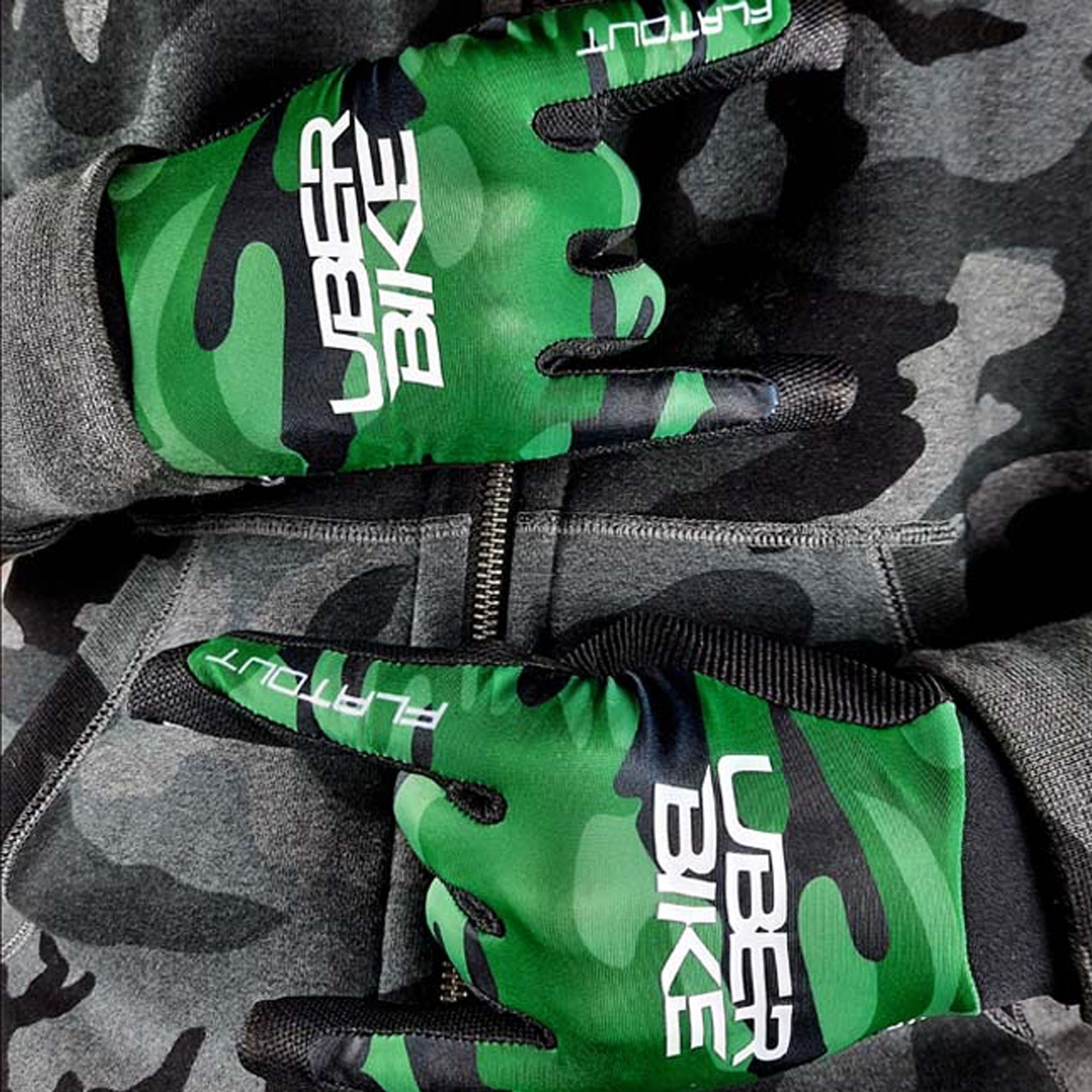 Green / black camouflage gloves with uberbike branding on a dark camouflage backgorund