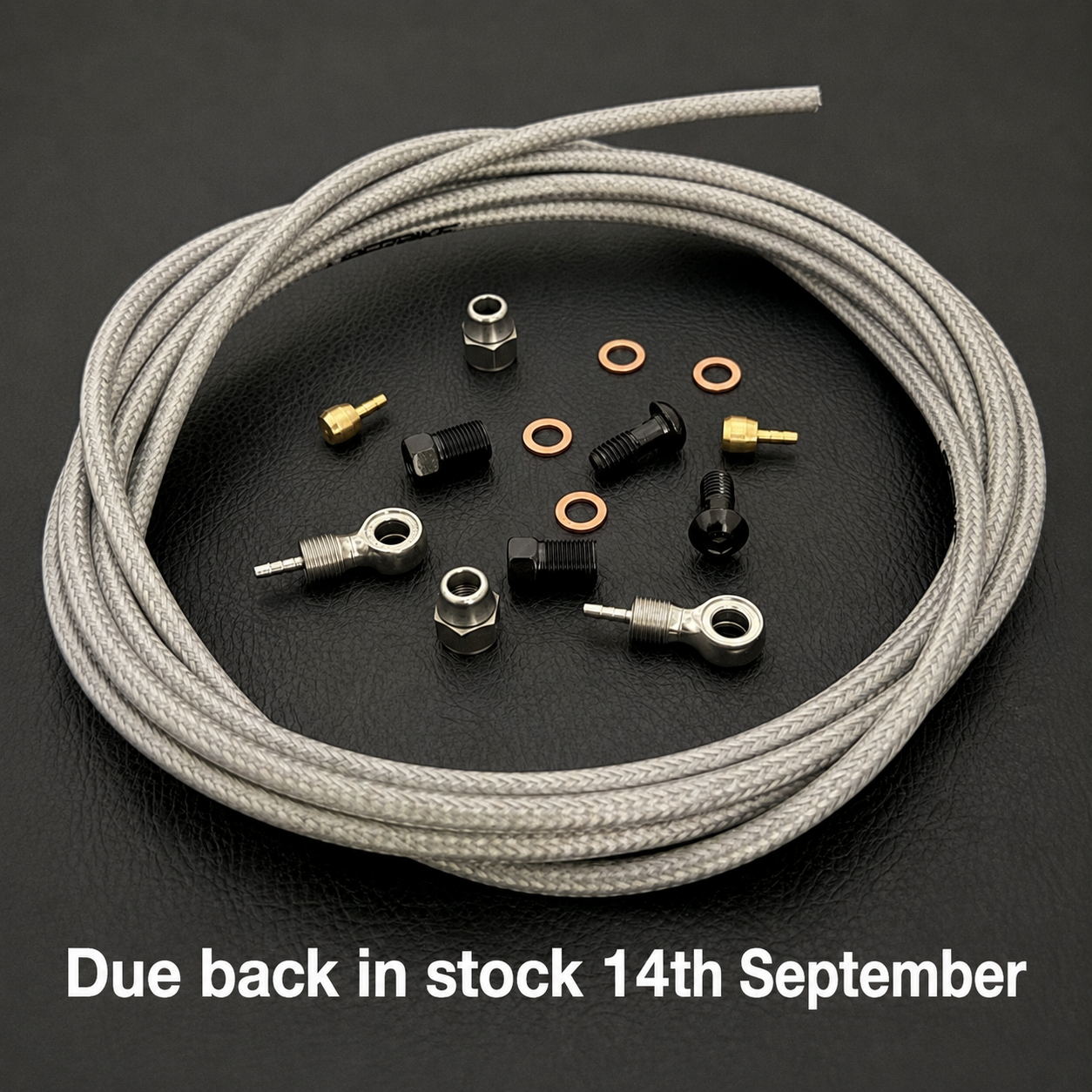 A coiled light silver braided shimano xtr brake cable with several small metal hardware components arranged on a dark textured surface. White text at the bottom reads 'Due back in stock 14th September'.